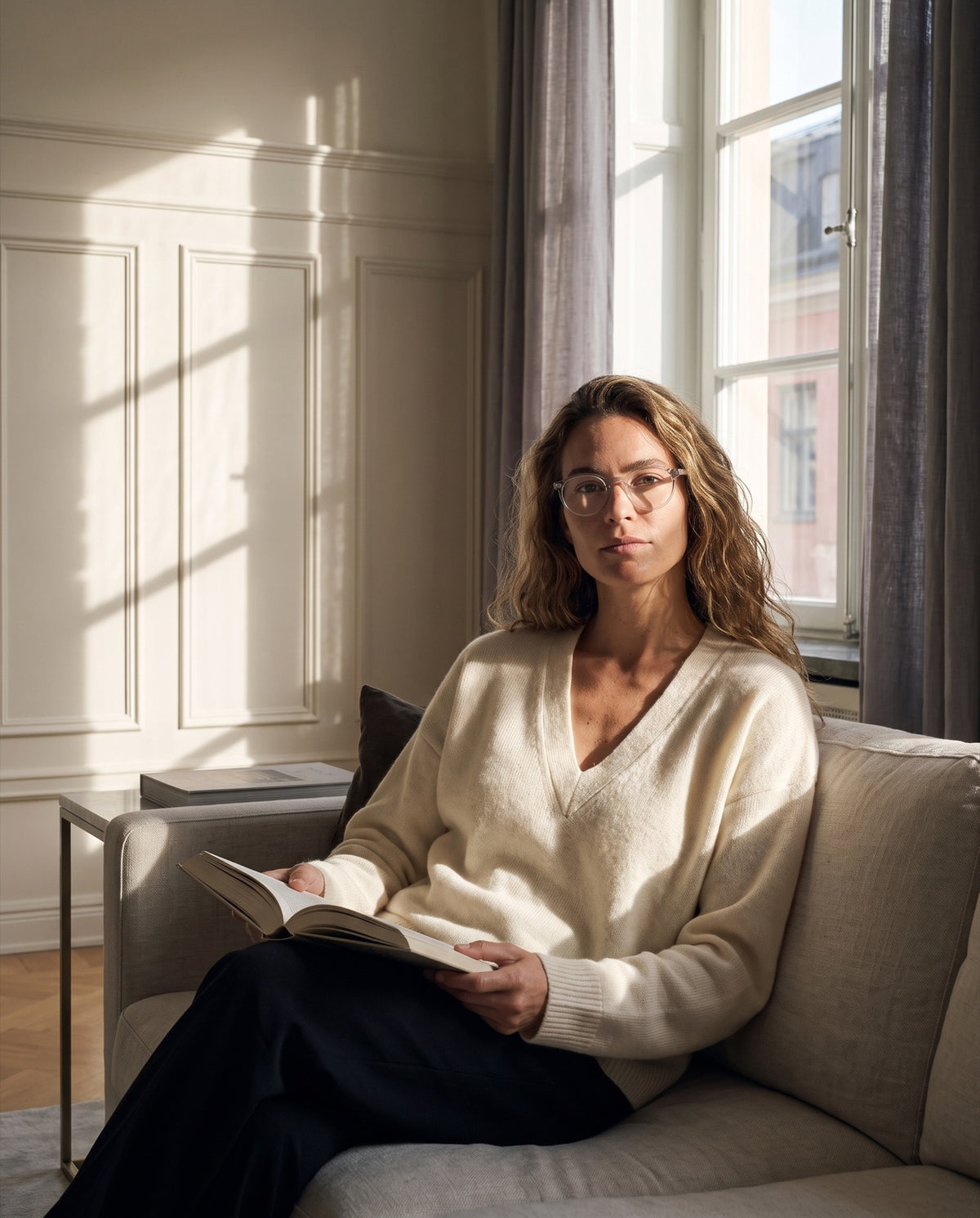 A woman reading on the sofa in low September light, wearing Emily Quartz readers.